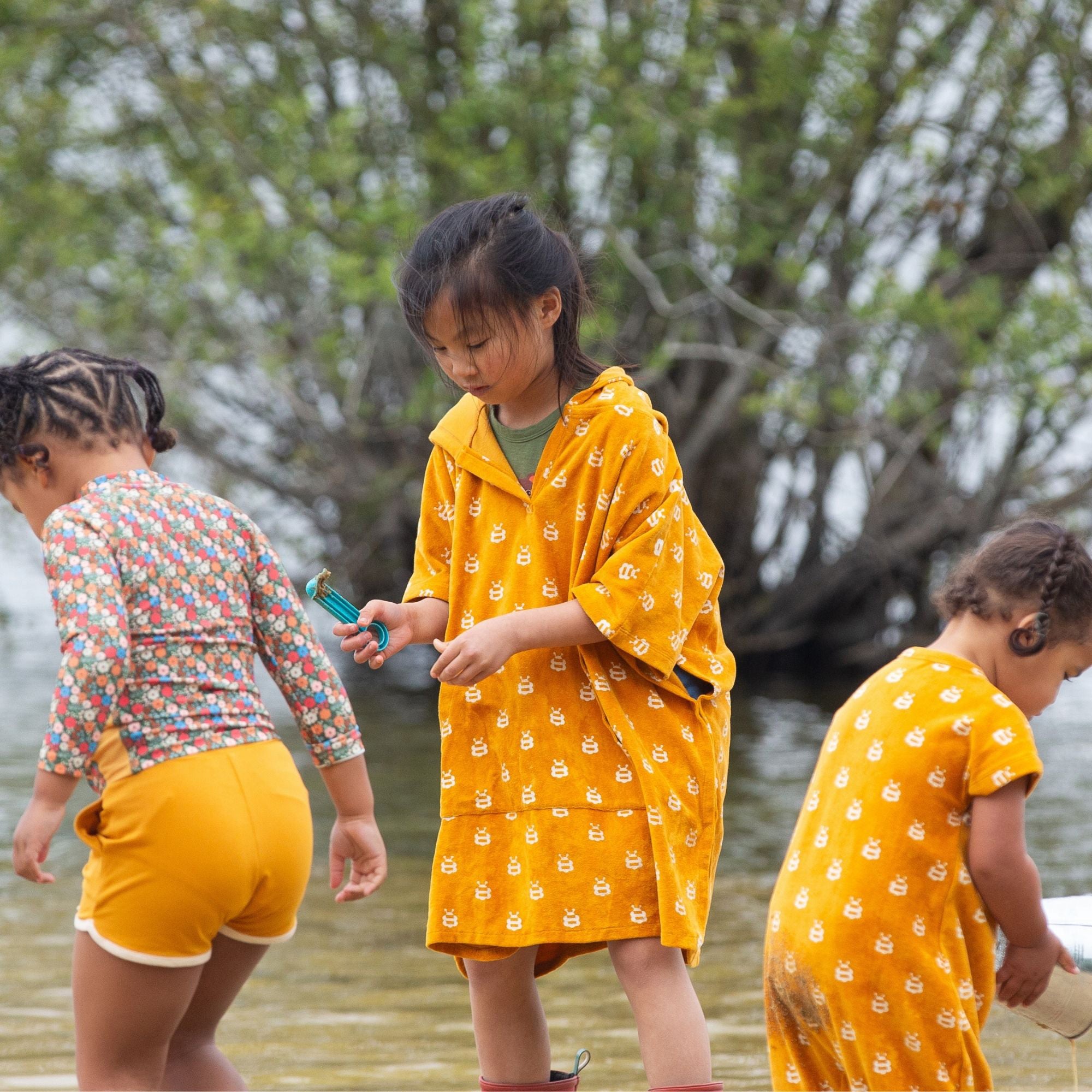  Children playing outdoors in Little Green Radicals swim wear,  one child is wearing the Little Green Radicals Children's Bees pattern Hooded organic cotton Beach Towel Poncho