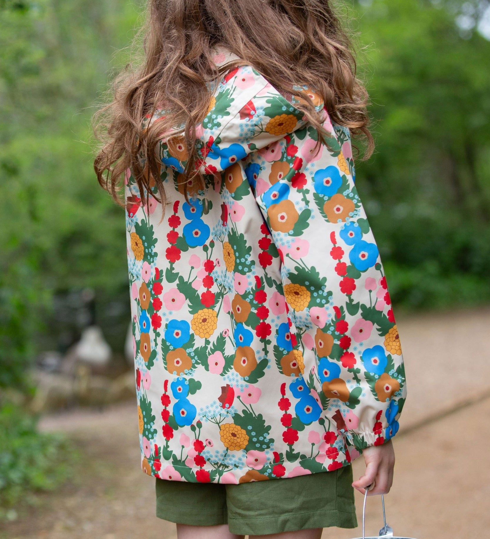 Little Green Radicals Child's Flora & Fauna vintage style flower print Waterproof Raincoat. The child is facing away from the camera showing a view of the back of the jacket.