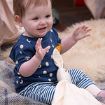 A baby wearing the Little Green Radicals  Full Moon T-Shirt & Jogger outfit set. The baby is sitting on a blanket with a cream coloured bunny comforter toy on their lap.  