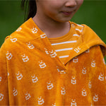 A close up of a child wearing the Little Green Radicals Children's Bees pattern Hooded organic cotton Beach Towel Poncho, the photo focuses on the neckline. 