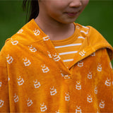 A close up of a child wearing the Little Green Radicals Children's Bees pattern Hooded organic cotton Beach Towel Poncho, the photo focuses on the neckline. 