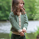 A child wearing the Little Green Radicals From One To Another Olive Green Striped Knitted Child's Organic Cotton Cardigan with green coloured shorts.