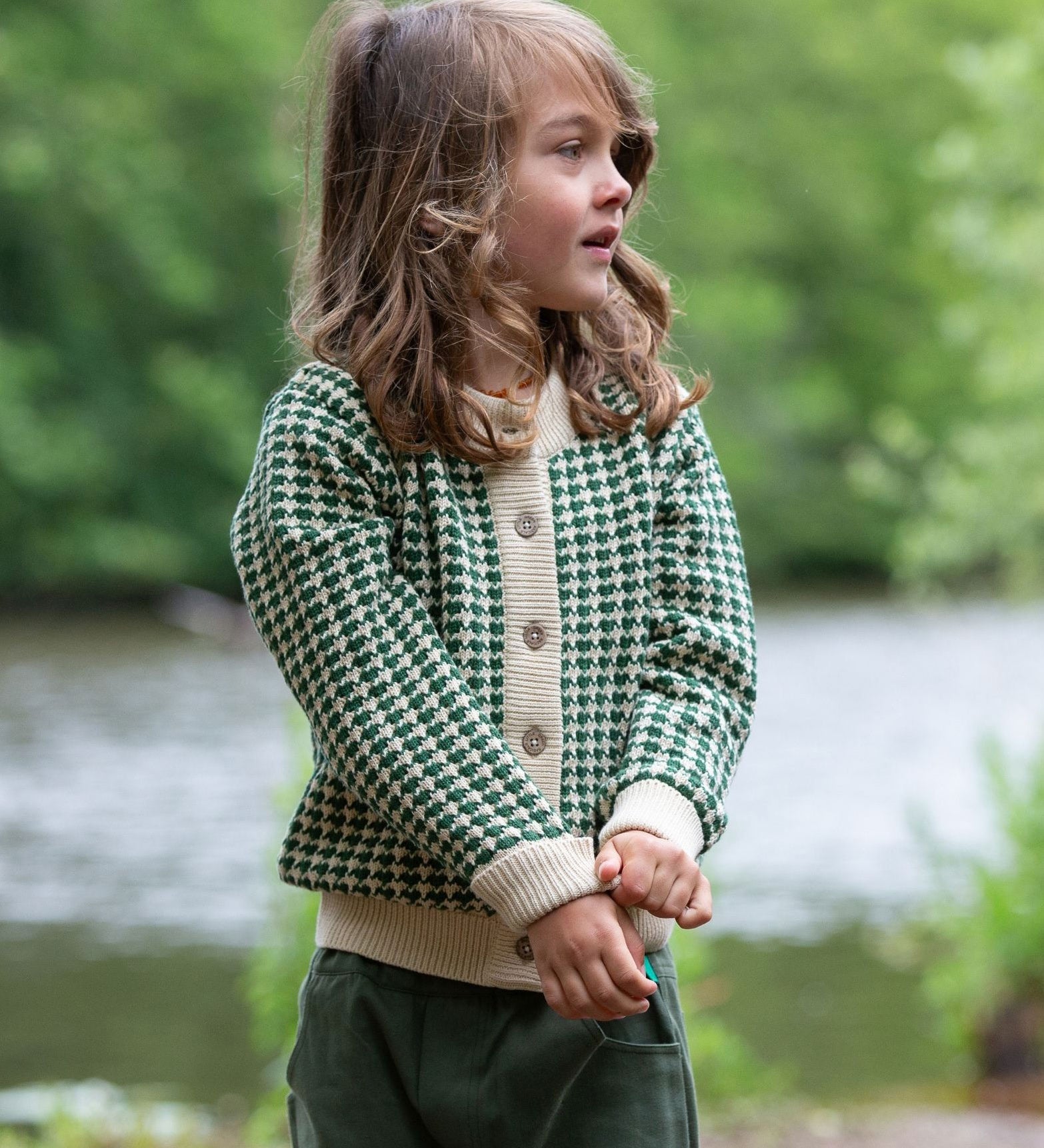 A child wearing the Little Green Radicals From One To Another Olive Green Striped Knitted Child's Organic Cotton Cardigan with green coloured shorts.