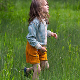 A child wearing the blue and white From One To Another Knitted Cardigan by Little Green Radicals with yellow gold coloured shorts. The child is running through long green grass.