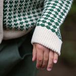 A close up of a child wearing the Little Green Radicals From One To Another Olive Green Striped Knitted Child's Organic Cotton Cardigan. The close up focuses in on the cardigan's sleeves. 