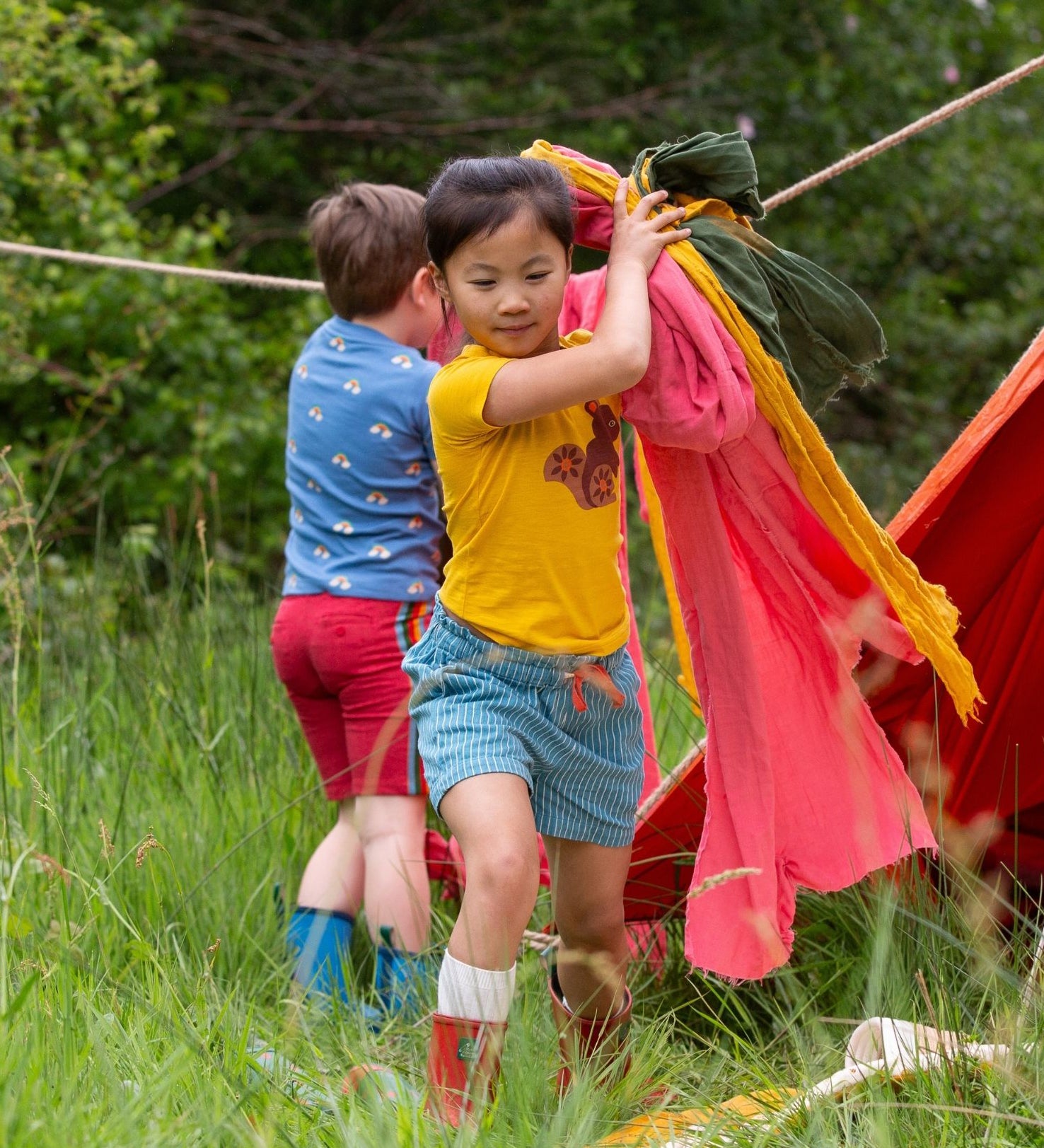 A child wearing the Little Green Radicals Yellow gold coloured Squirrel t-shirt with blue striped shorts. 