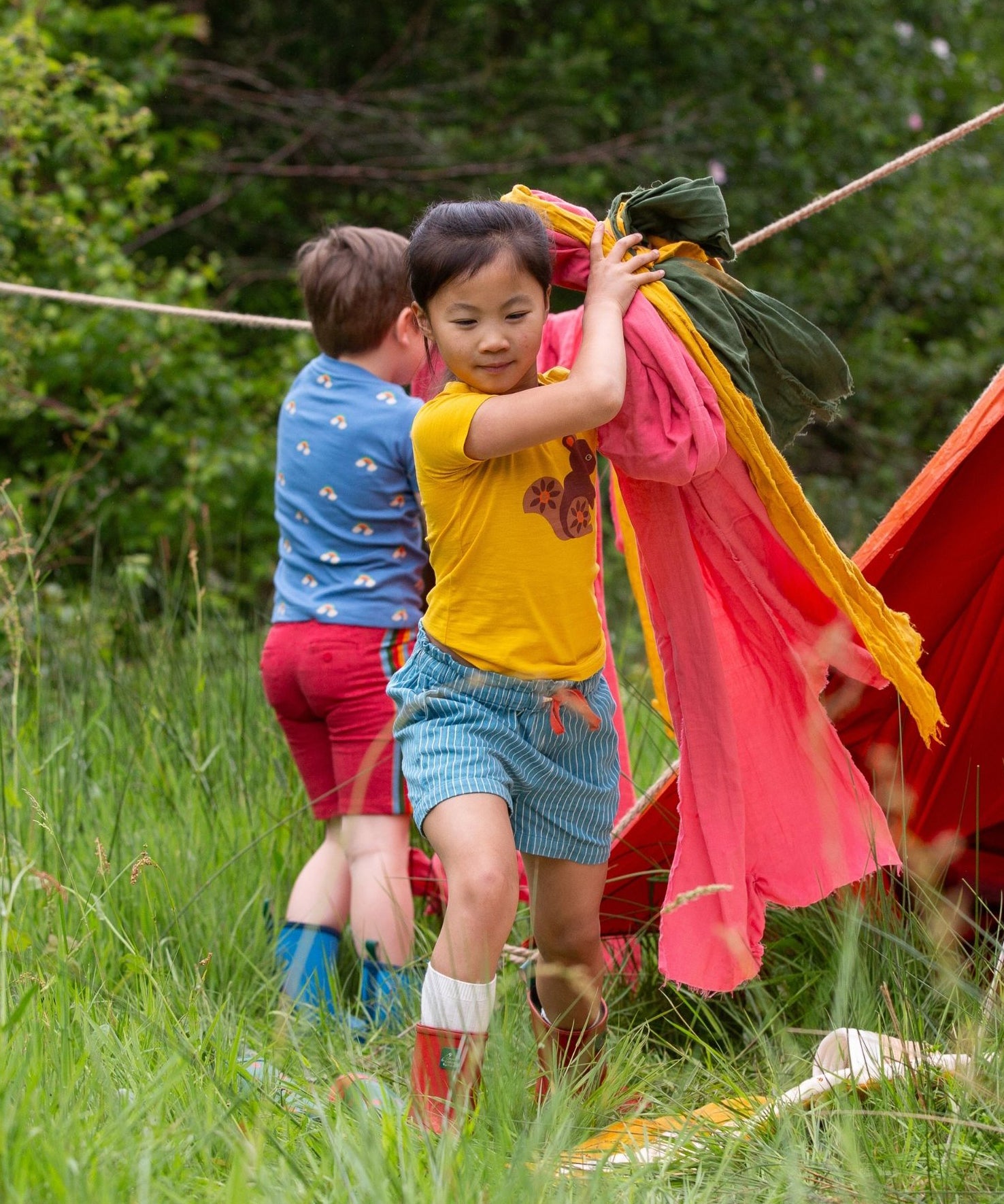 A child wearing the Little Green Radicals Yellow gold coloured Squirrel t-shirt with blue striped shorts. 