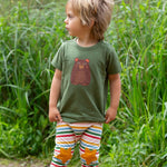 A child wearing the Little Green Radicals Kids Organic Cotton Green Bear Short Sleeve T-Shirt with rainbow striped star knee patch joggers.