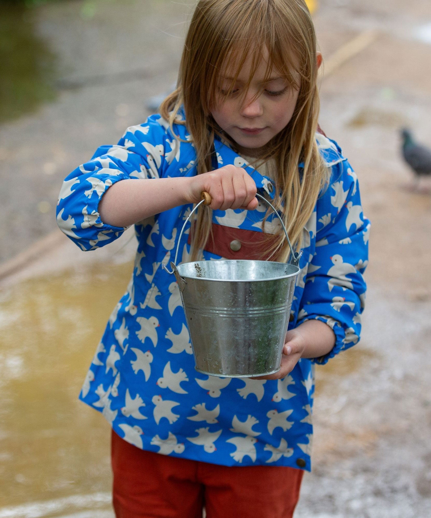 A front view of a child wearing the Little Green Radicals Diving And Splashing Blue Recycled Waterproof Kids Packable Anorak.