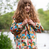 A child wearing the Little Green Radicals Child's Flora & Fauna vintage style flower print Waterproof Raincoat