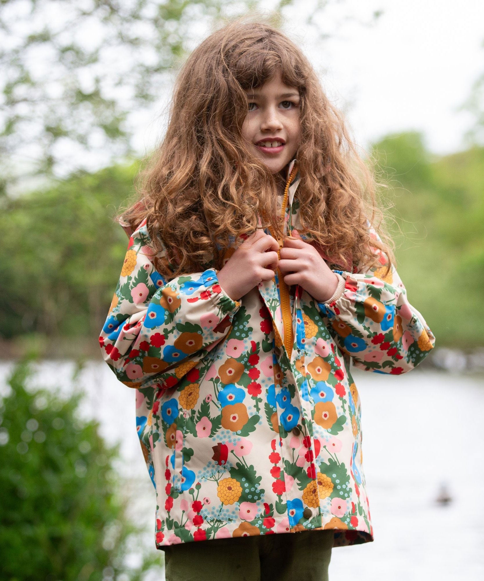 A child wearing the Little Green Radicals Child's Flora & Fauna vintage style flower print Waterproof Raincoat