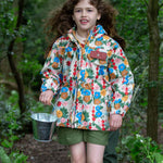 A child wearing the Little Green Radicals Child's Flora & Fauna vintage style flower print Waterproof Raincoat with green coloured shorts