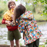 A child wearing the Little Green Radicals Child's Flora & Fauna vintage style flower print Waterproof Raincoat, facing away from the camera showing the back of the jacket and the hood. 