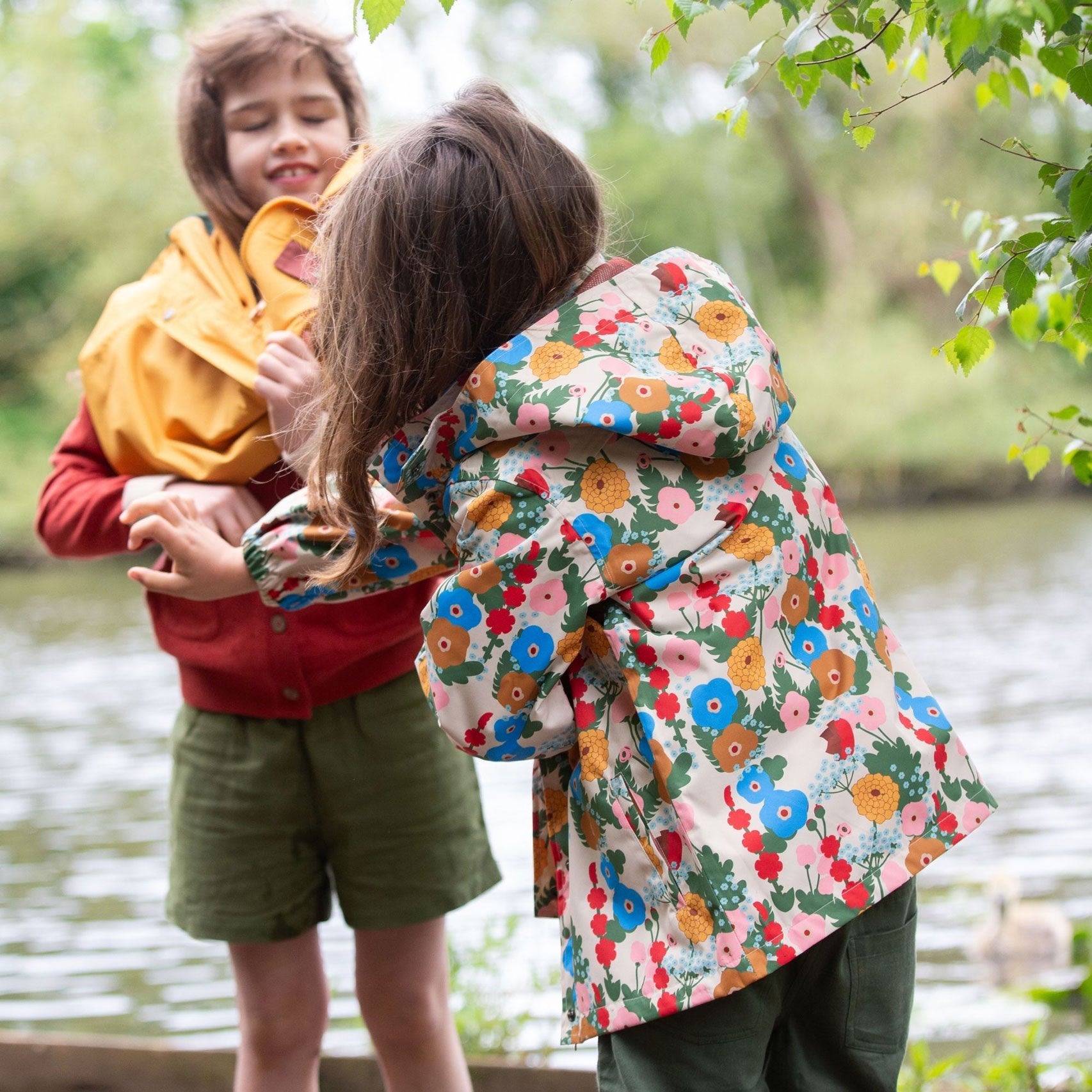 A child wearing the Little Green Radicals Child's Flora & Fauna vintage style flower print Waterproof Raincoat, facing away from the camera showing the back of the jacket and the hood. 