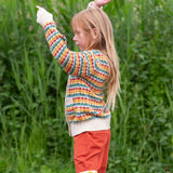 A child wearing the Little Green Radicals From One To Another Rainbow Days Organic Cotton Knitted Cardigan with red coloured shorts.