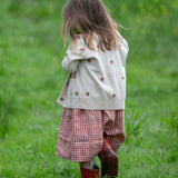 A child wearing the Little Green Radicals organic From One To Another Strawberry Days print child's Knitted Cardigan. The child is facing away from the camera showing the back of the cardigan