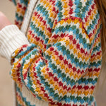 A close up of a child wearing the Little Green Radicals From One To Another Rainbow Days Organic Cotton Knitted Cardigan