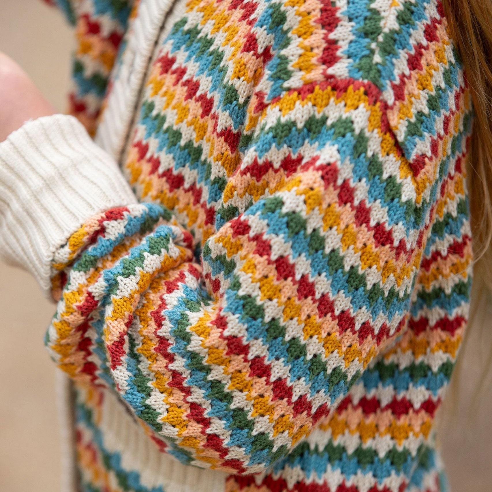 A close up of a child wearing the Little Green Radicals From One To Another Rainbow Days Organic Cotton Knitted Cardigan