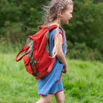 A side view of a child wearing the Little Green Radicals Kids Ready For Adventure Yellow Stars print red and green Backpack on their back showing the side of the bag. 