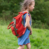 A side view of a child wearing the Little Green Radicals Kids Ready For Adventure Yellow Stars print red and green Backpack on their back showing the side of the bag. 