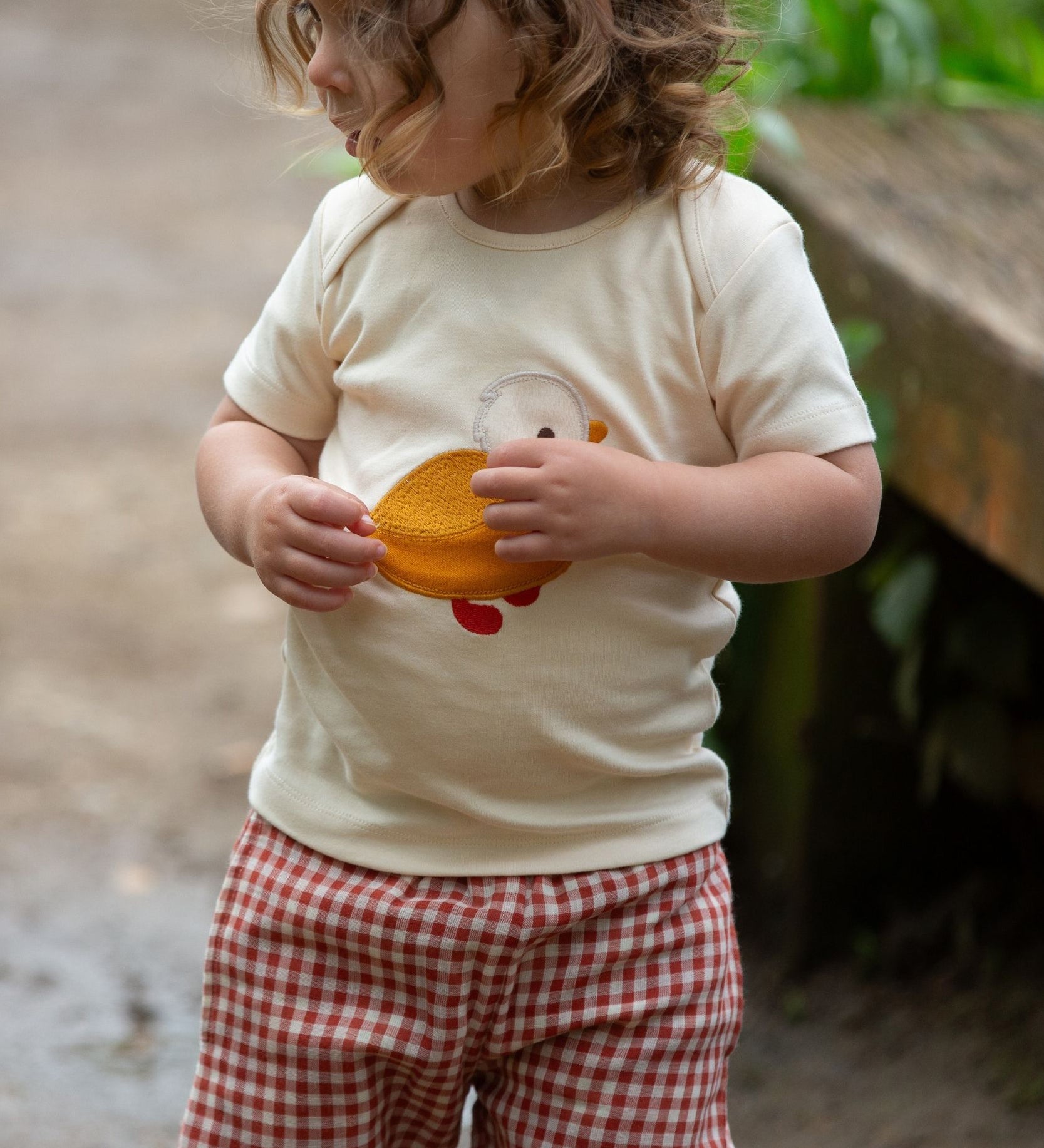 A child wearing the Little Green Radicals Little Duck Applique Short Sleeve T-Shirt with .ed and white gingham shorts. 