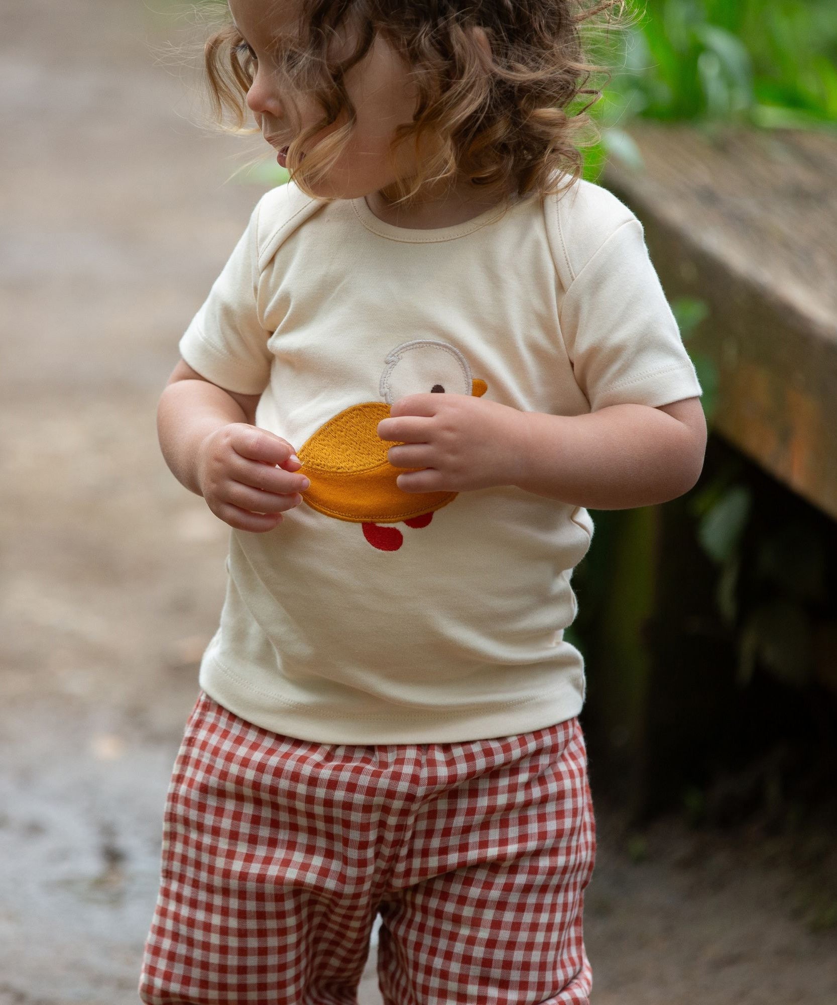 A child wearing the Little Green Radicals Little Duck Applique Short Sleeve T-Shirt with .ed and white gingham shorts. 