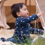 A baby wearing the Little Green Radicals Full Moon Organic Cotton Babygrow sitting on the grass. 