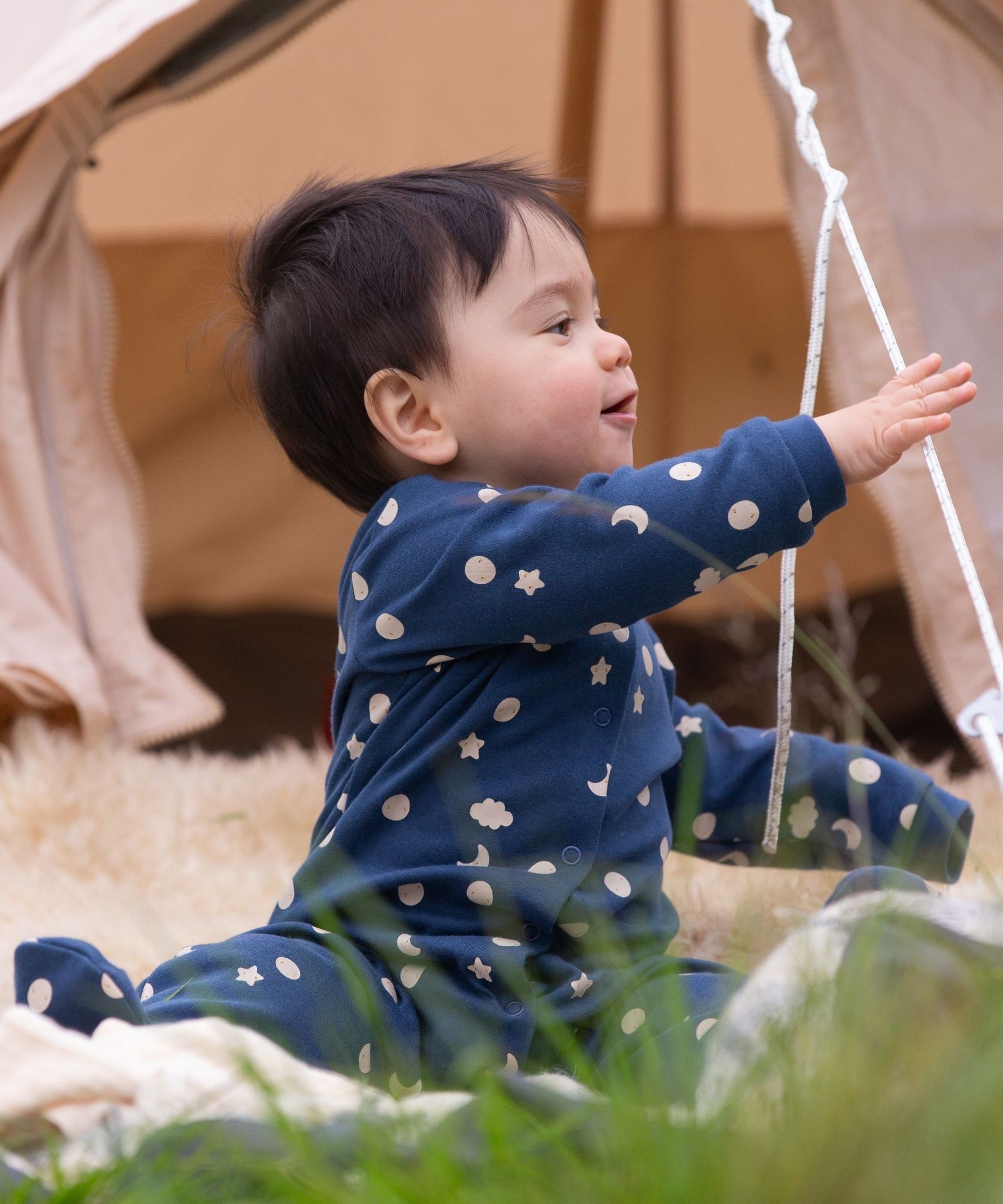 A baby wearing the Little Green Radicals Full Moon Organic Cotton Babygrow sitting on the grass. 