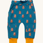 Little Green Radicals Organic Cotton Kids Comfy Joggers with a brown Teddy Bears print on a blue coloured background. The joggers have yellow gold coloured cuffs.