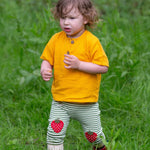 A child wearing the Little Green Radicals Strawberry Knee Patch Green and Cream Striped Organic Cotton Joggers with a bright yellow gold coloured short sleeved t-shirt.