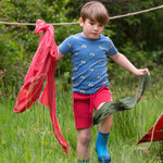 A child wearing the Little Green Radicals Red Comfy Jogger Shorts with a blue rainbow short sleeved t-shirt. The child is running through long green grass.