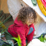 A child wearing the Little Green Radicals Child's Red Organic Quarter Zip Hoodie with green shorts