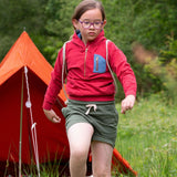 A child wearing the Little Green Radicals Child's Red Organic Quarter Zip Hoodie with green shorts. An orange tenet can be seen in the back ground.