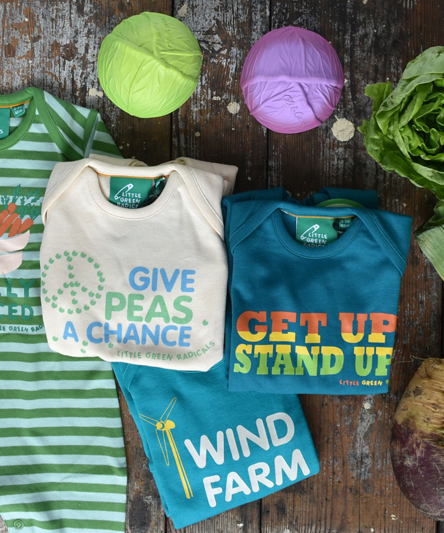 A flatlay featuring the four Little Green Radicals slogan playsuits. Three are folded up with one just off to the side laid out flat 