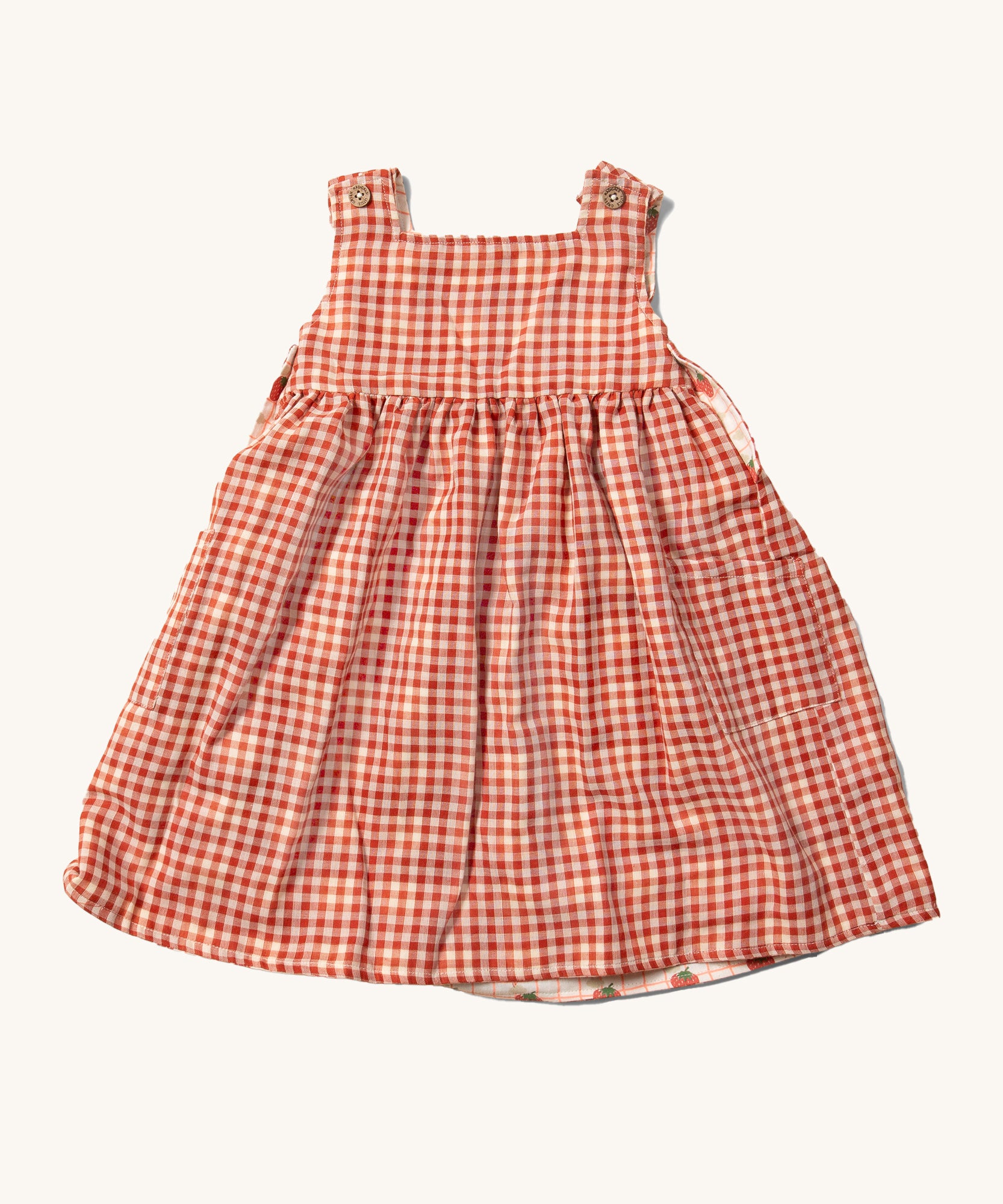 Little Green Radicals Child's Organic Cotton Strawberry Days Reversible Pinny Dress shown with the red gingham side on the outside.