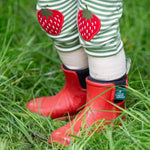 A close up of a child wearing the Little Green Radicals Children's Strawberry Knee Patch Green and Cream Striped Organic Cotton Joggers with red wellington boots