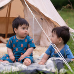 A child sitting in front of a bell tent wearing the Little Green Radicals Teddy Bears Organic Cotton Shortie Romper. 