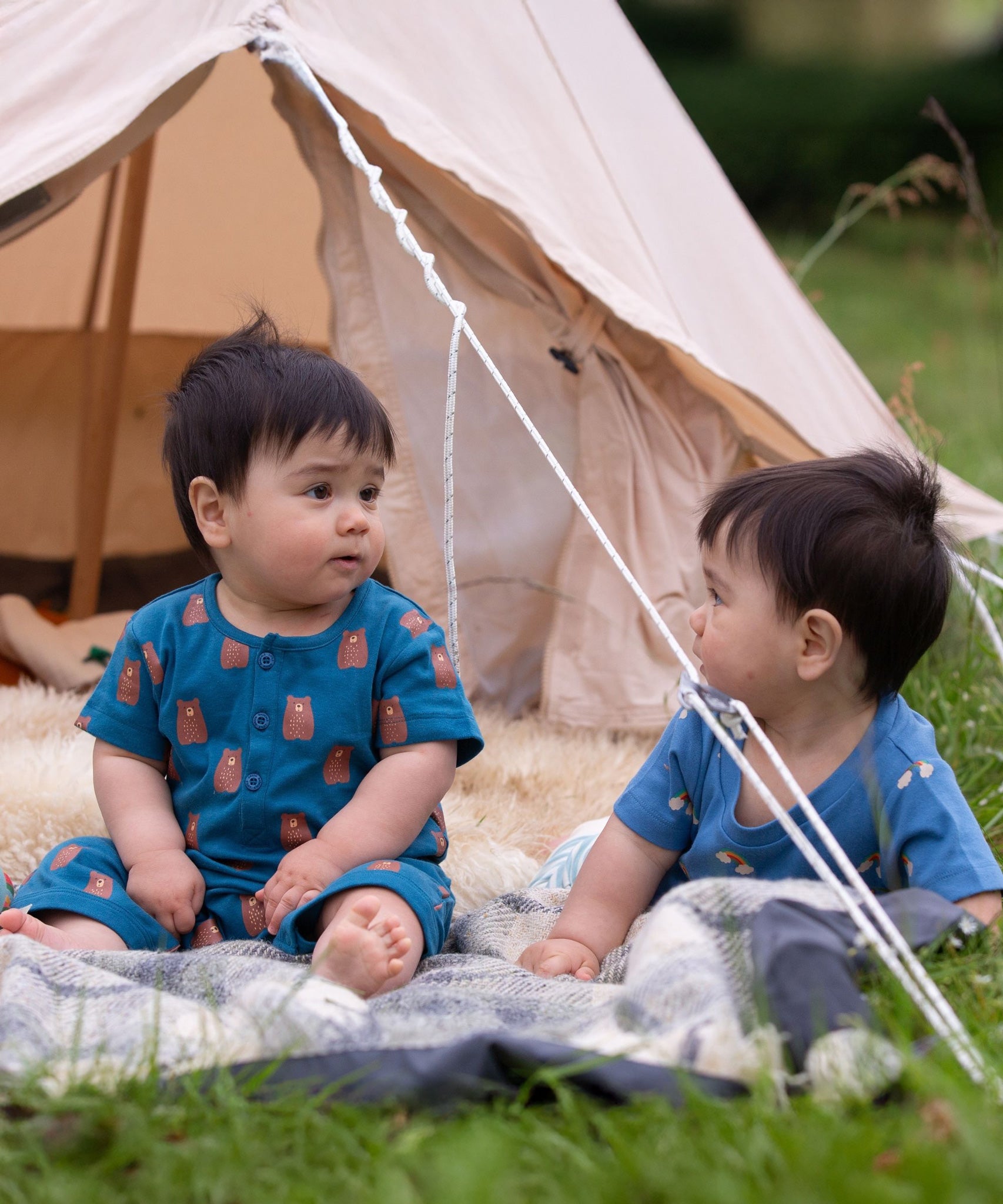 A child sitting in front of a bell tent wearing the Little Green Radicals Teddy Bears Organic Cotton Shortie Romper. 