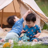 Two young children sitting in front of a bell tent one is wearing the Little Green Radicals Teddy Bears Organic Cotton Shortie Romper the other is wearing the Blue Rainbow playset. 