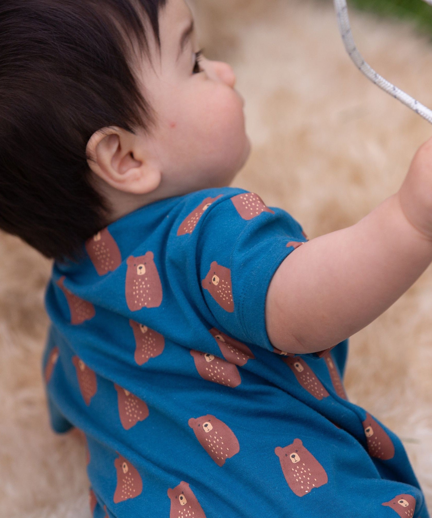 A close up of a child wearing the Little Green Radicals Teddy Bears Organic Cotton Shortie Romper. 