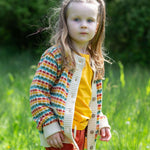 A child wearing the Little Green Radicals From One To Another Rainbow Days Organic Cotton Knitted Cardigan with red shorts.