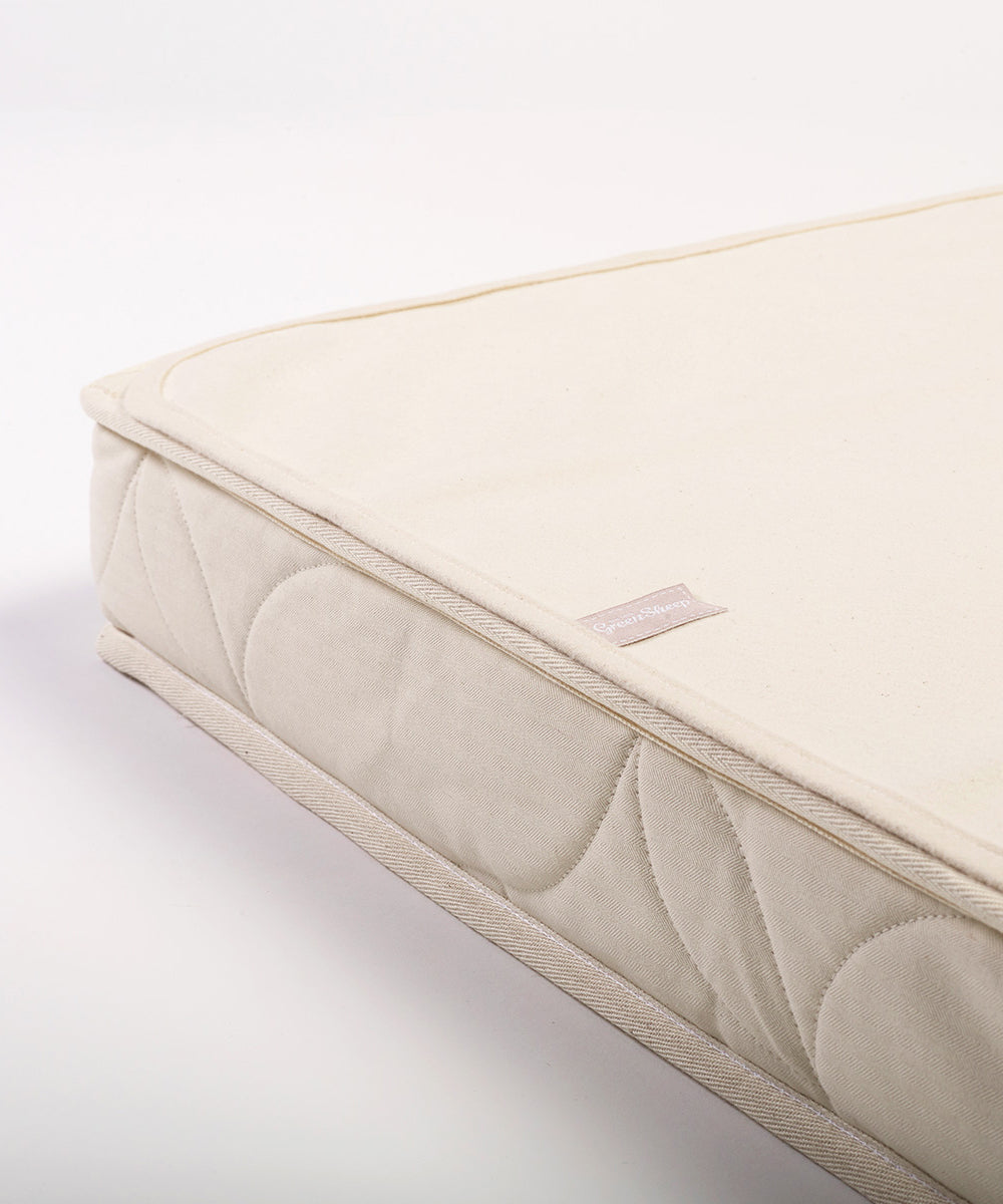 A close up of a Little Green Sheep Organic Cot Mattress Protector placed on a matress