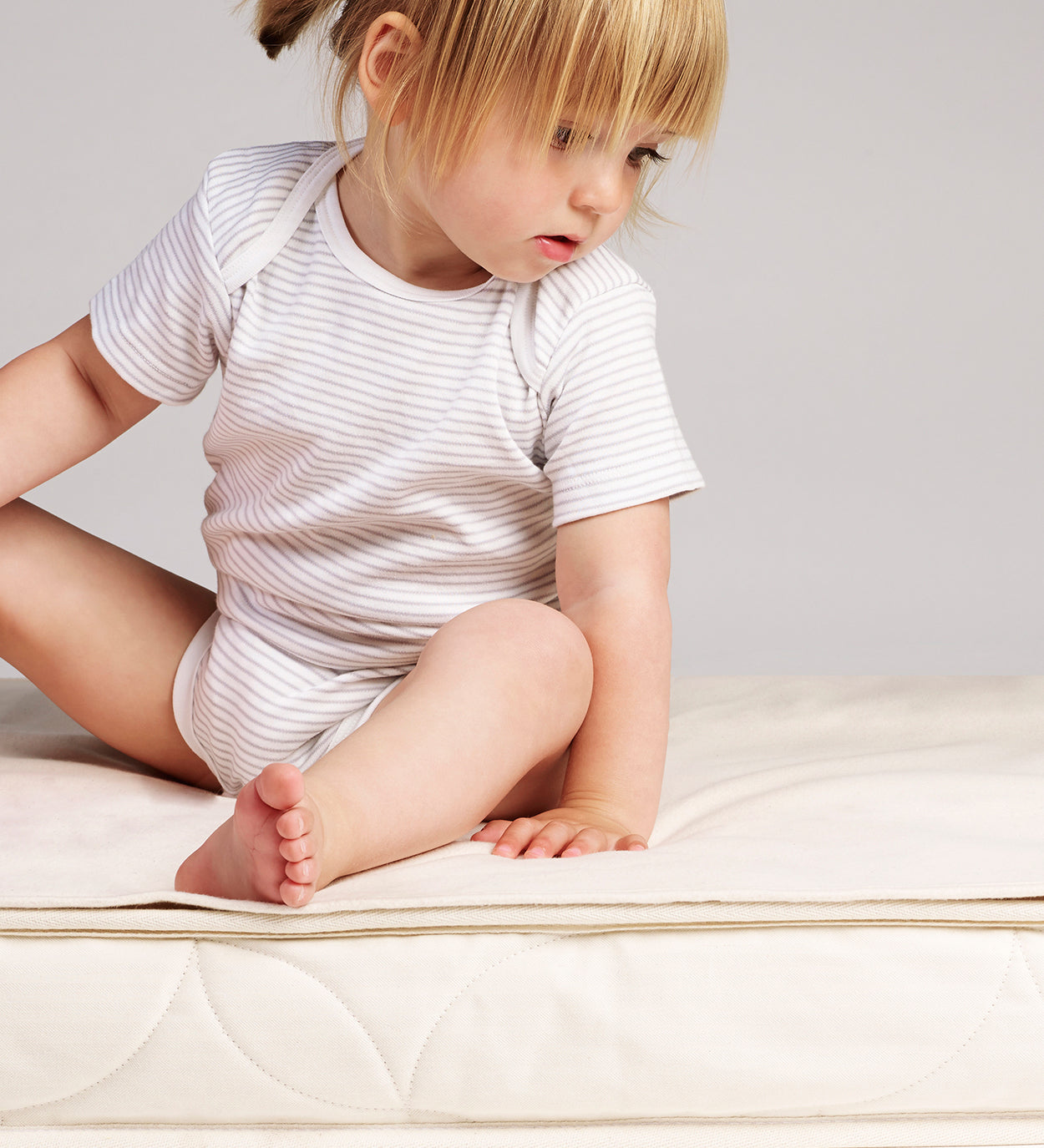 a small child sitting on a cot mattress which has a Little Green Sheep Organic Cot Mattress Protector placed on top