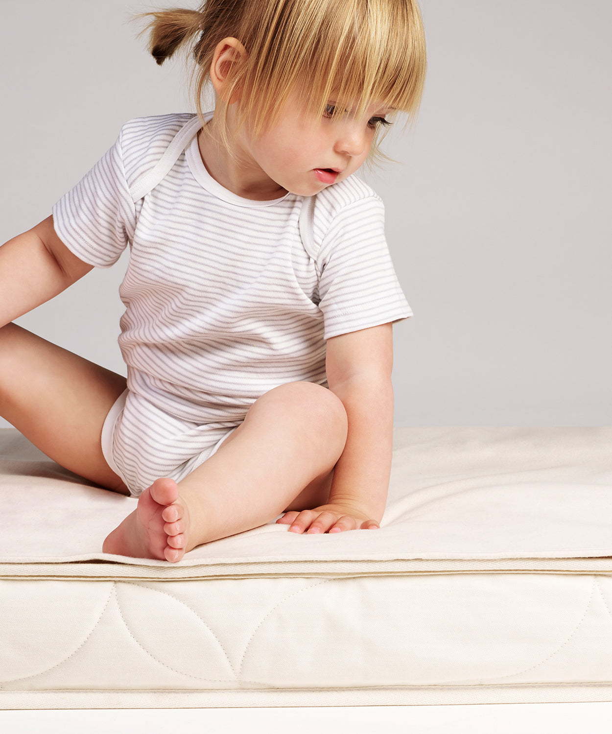 a small child sitting on a cot mattress which has a Little Green Sheep Organic Cot Mattress Protector placed on top