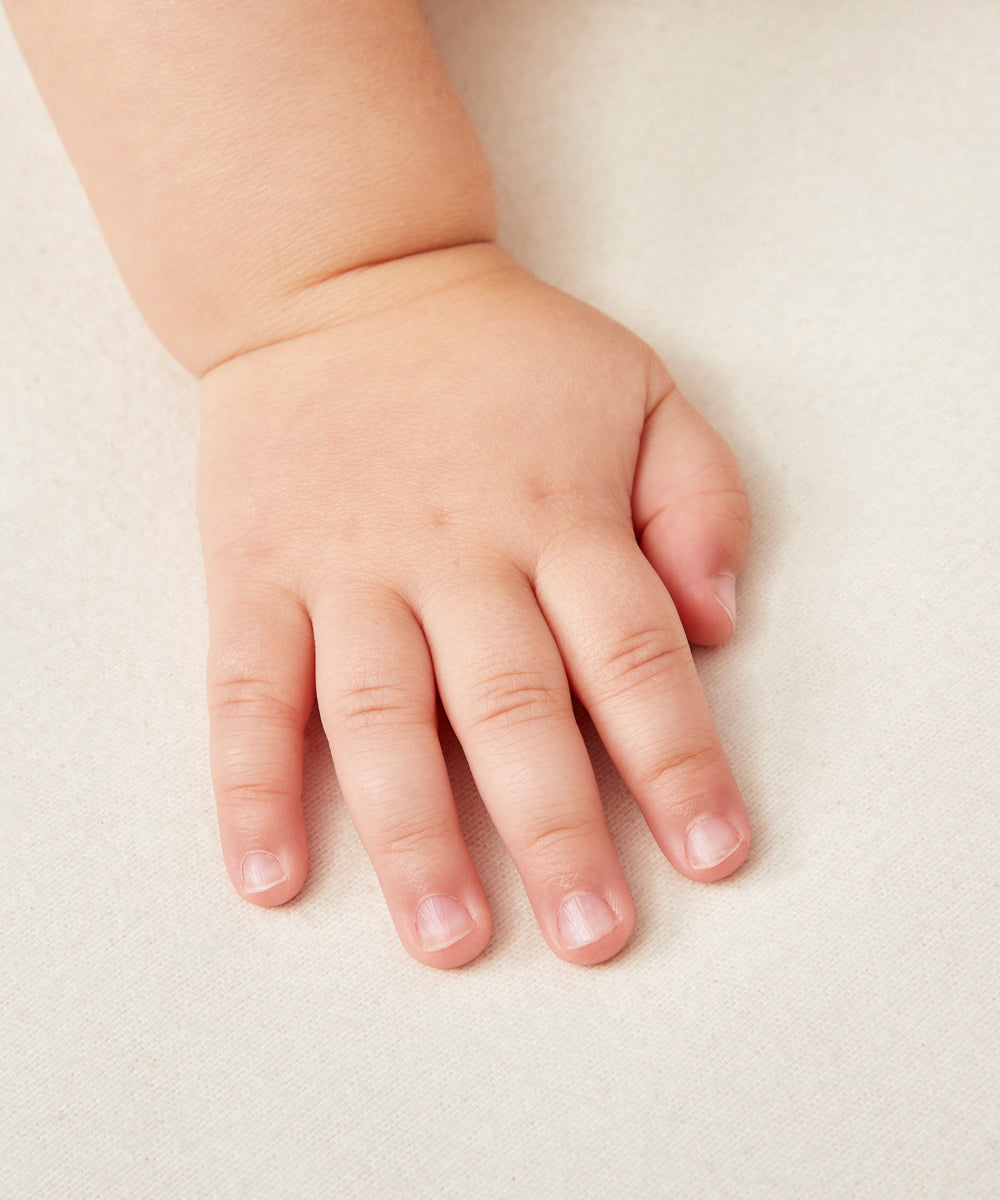 A close up of a baby's hand on a Little Green Sheep Organic Moses Basket / Pram Mattress Protector