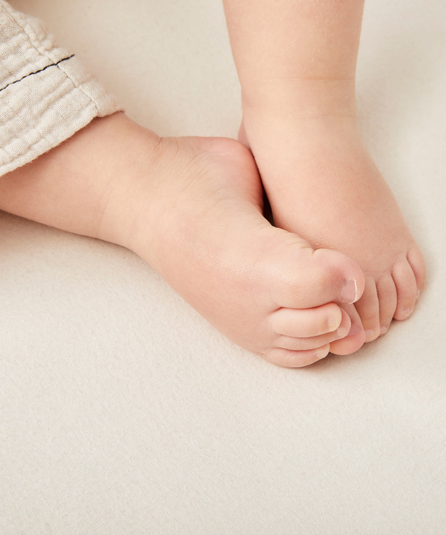 A close up of a child's feet on a Little Green Sheep Organic Cot Mattress Protector