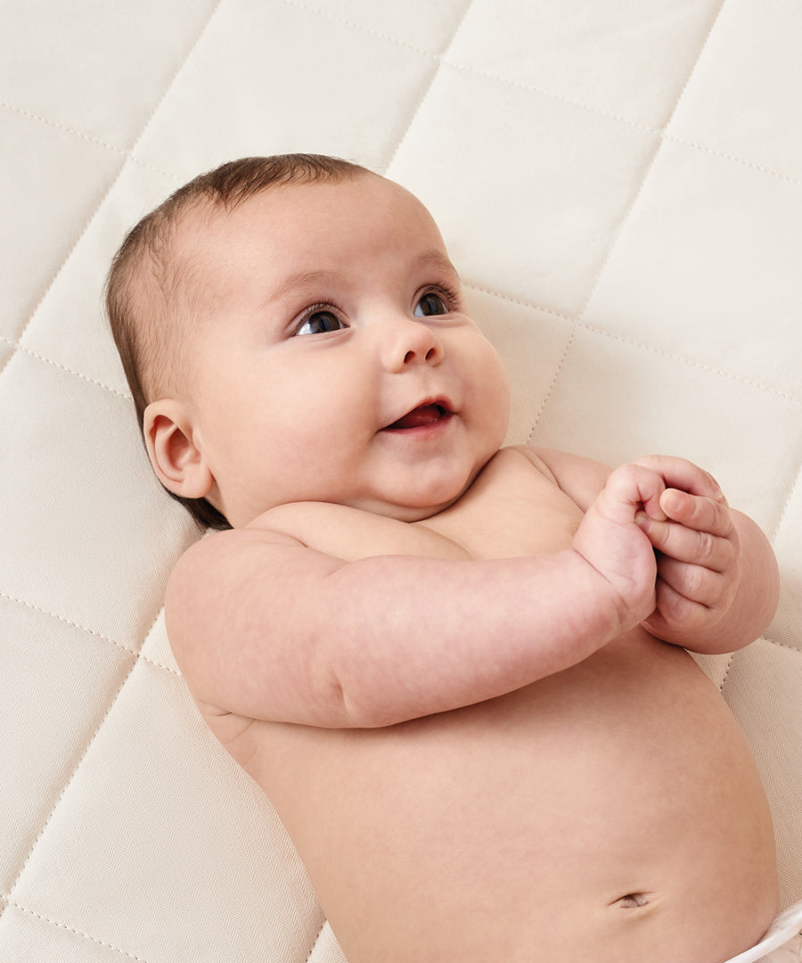 A baby laying down on a Little Green Sheep Natural Crib Mattress for Snuzpod4 