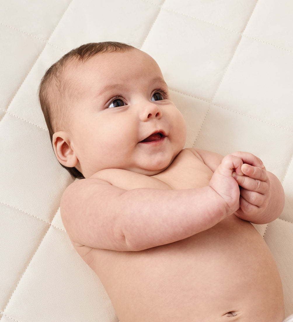 A baby laying down on a Little Green Sheep Natural Crib Mattress for Snuzpod4 