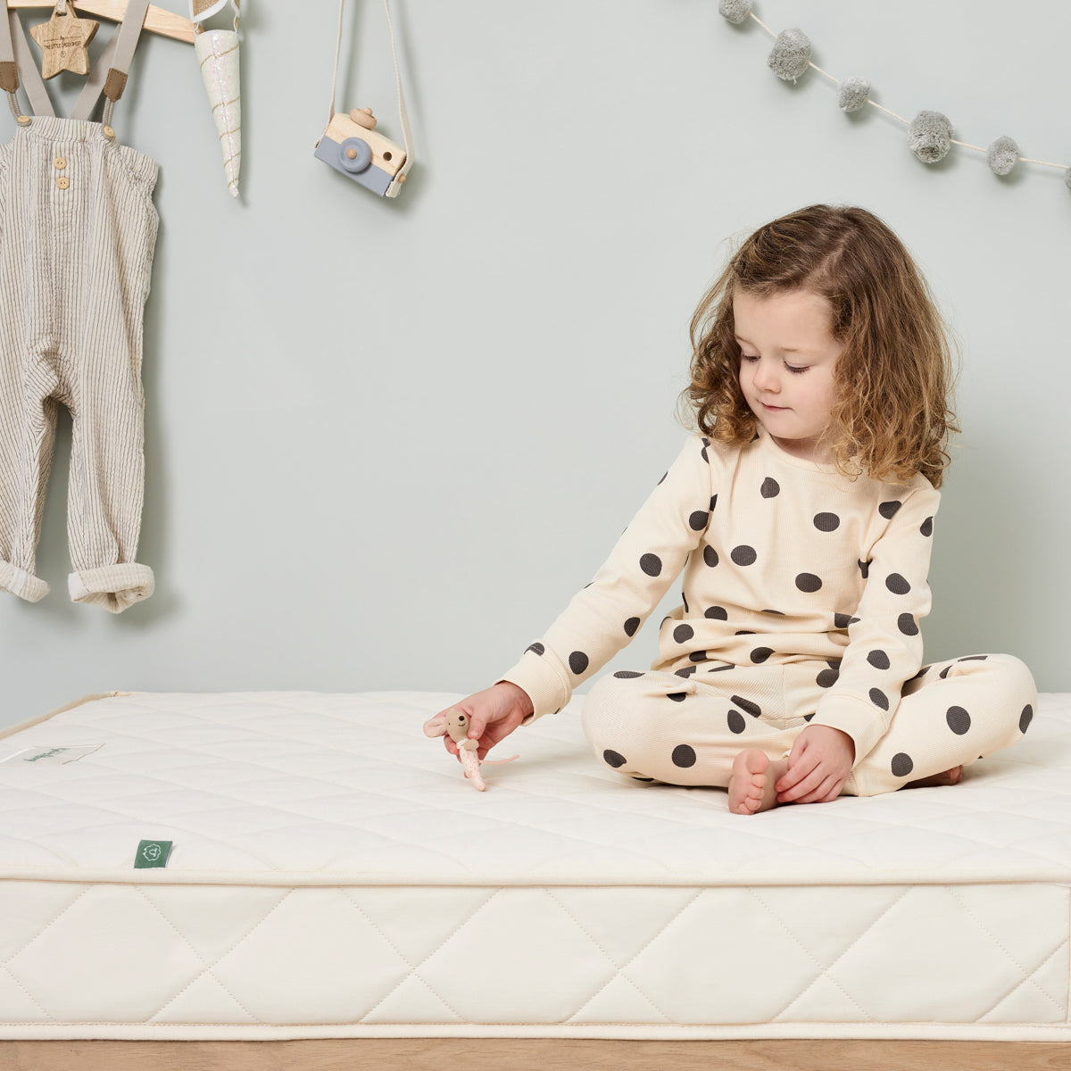 A child with shoulder length curly hair wearing spot print pyjamas sitting with their legs crossed on a Little Green Sheep mattress 