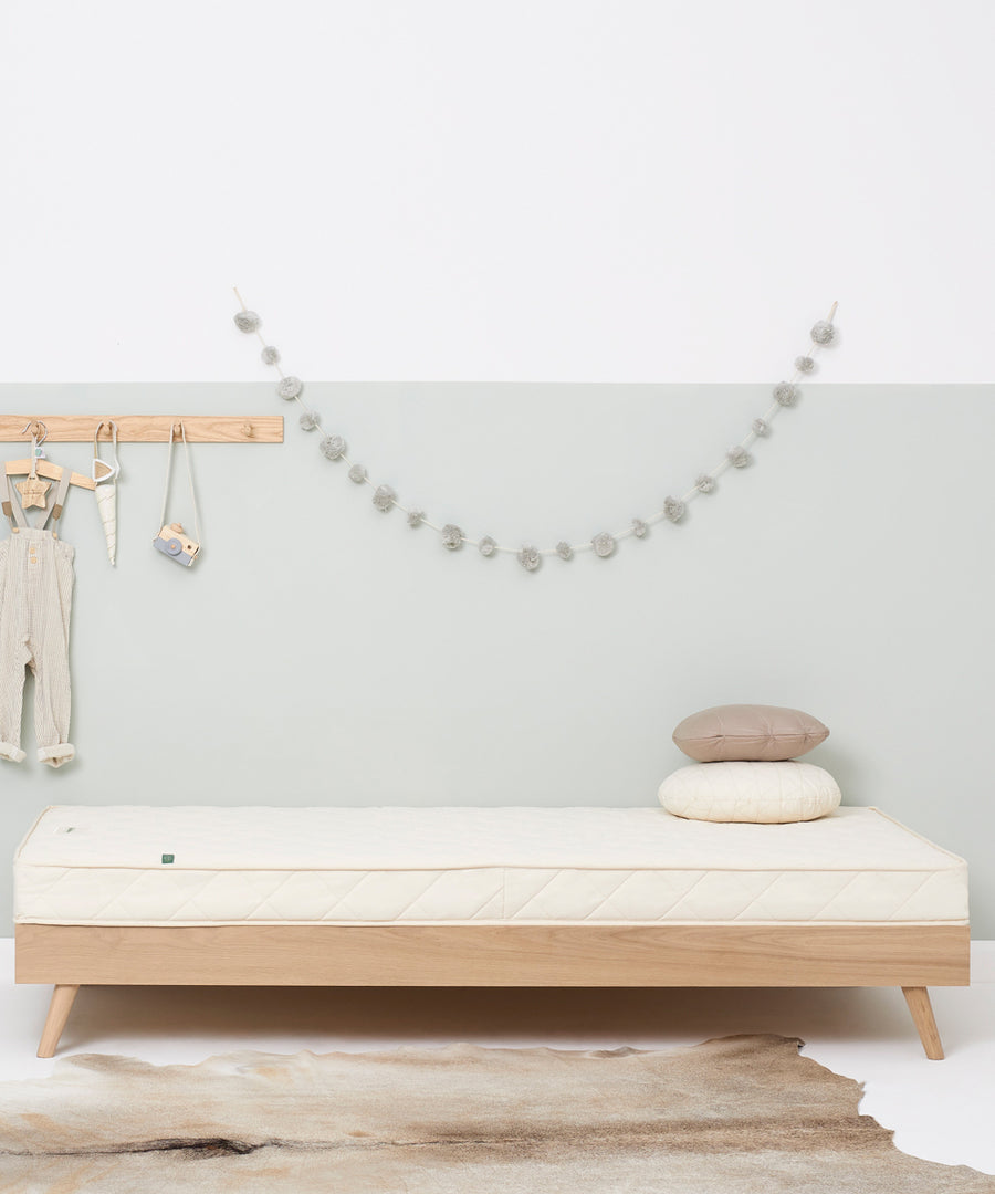 A wooden trundle bed with a Little Green Sheep atress on it. The bed is in a bedroom with walls painted white and light green.